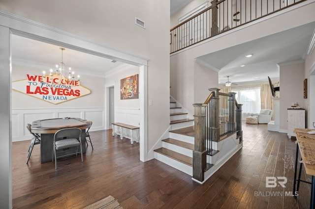 stairs with crown molding, ceiling fan with notable chandelier, and hardwood / wood-style flooring