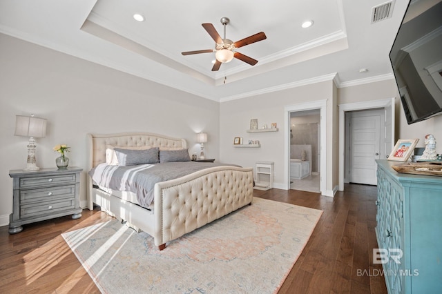 bedroom with ceiling fan, ensuite bathroom, a tray ceiling, dark wood-type flooring, and ornamental molding