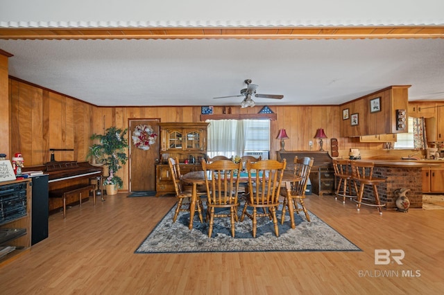 dining area featuring ceiling fan, wood-type flooring, ornamental molding, and wood walls