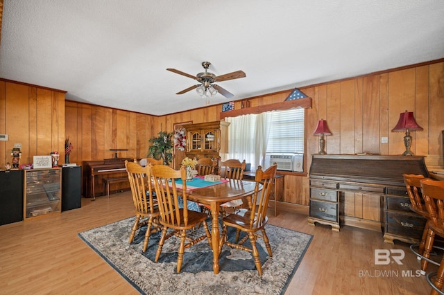 dining area with ceiling fan, cooling unit, wooden walls, and light hardwood / wood-style flooring