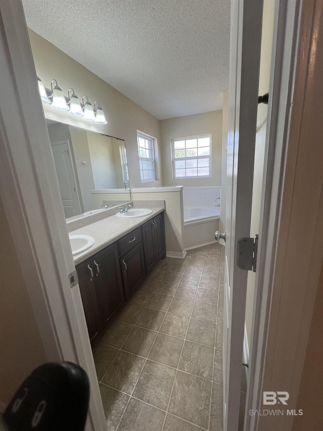 bathroom featuring a tub to relax in, vanity, and a textured ceiling