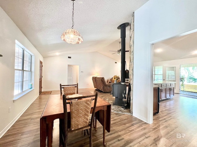 dining room with a textured ceiling, a wood stove, vaulted ceiling, and light wood-type flooring