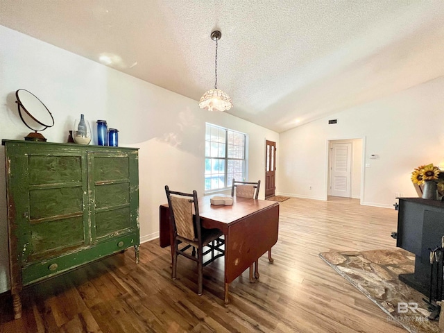 dining room with a chandelier, hardwood / wood-style floors, a textured ceiling, and vaulted ceiling