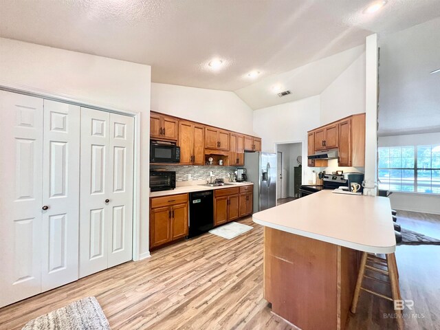 kitchen featuring kitchen peninsula, a kitchen breakfast bar, light wood-type flooring, sink, and black appliances