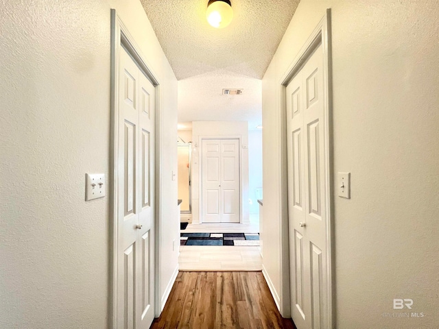 hallway with a textured ceiling, dark hardwood / wood-style flooring, and lofted ceiling