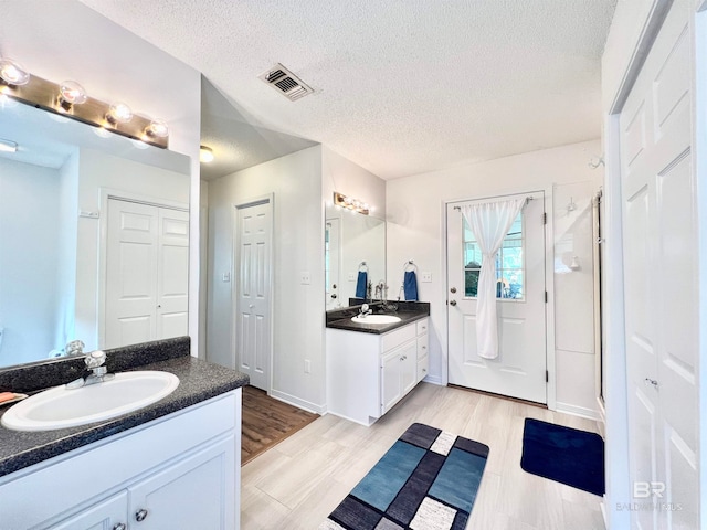 bathroom with vanity, wood-type flooring, a textured ceiling, and walk in shower