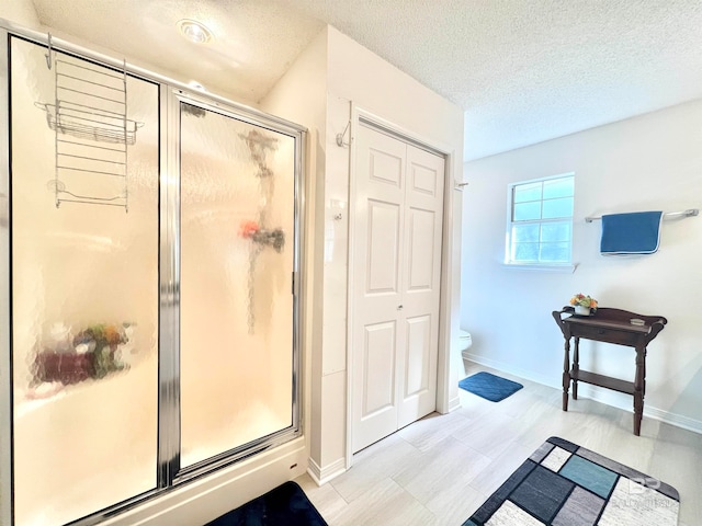 bathroom with toilet, a shower with door, and a textured ceiling