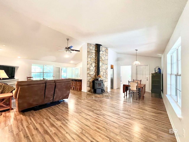 living room featuring lofted ceiling, ceiling fan, a wood stove, and light hardwood / wood-style flooring