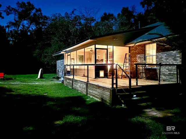 back house at twilight with a lawn and a sunroom