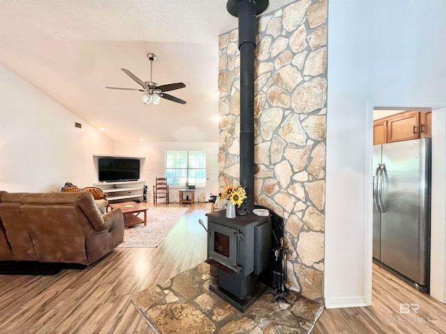 living room featuring light wood-type flooring, a textured ceiling, ceiling fan, a wood stove, and lofted ceiling