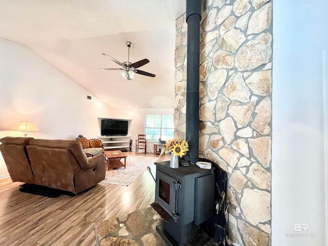 living room featuring a wood stove, ceiling fan, light hardwood / wood-style flooring, a textured ceiling, and vaulted ceiling