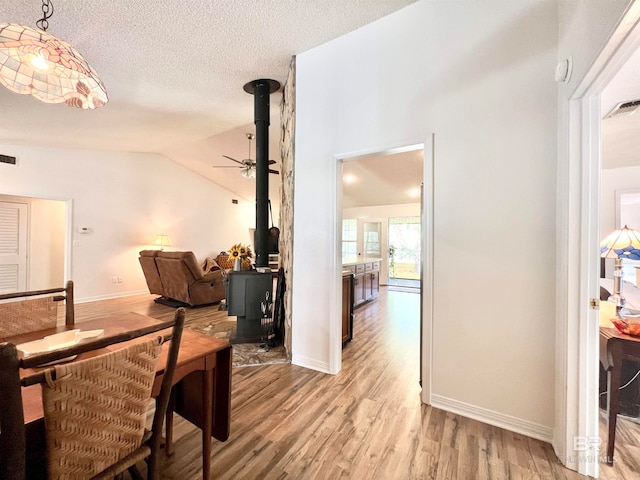 dining space with a wood stove, a textured ceiling, high vaulted ceiling, and light hardwood / wood-style flooring