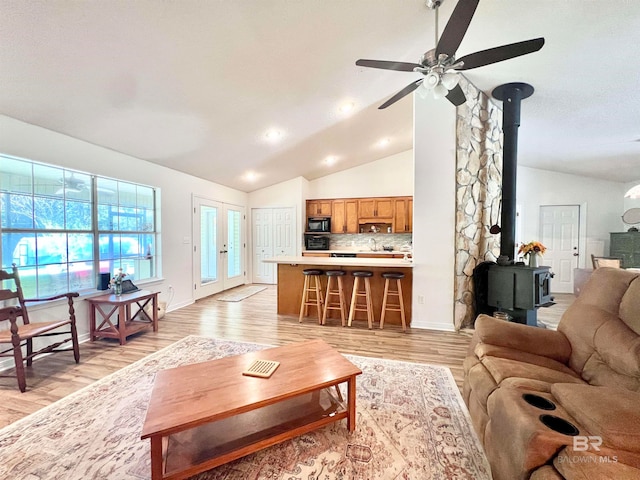 living room featuring light wood-type flooring, a wood stove, ceiling fan, and lofted ceiling