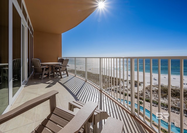 balcony with a water view, outdoor dining area, and a view of the beach