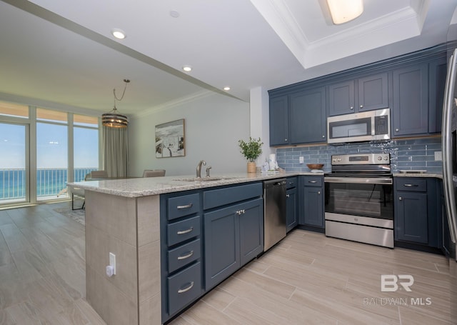 kitchen featuring appliances with stainless steel finishes, light stone countertops, a sink, a peninsula, and ornamental molding