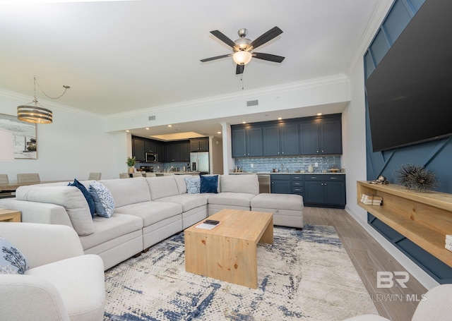 living room with crown molding, a ceiling fan, visible vents, and light wood-type flooring