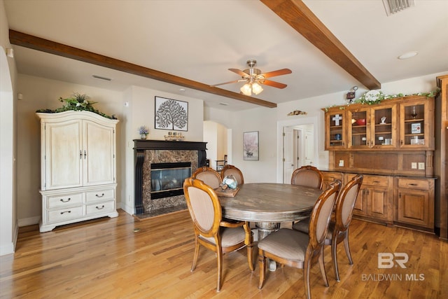 dining space with beamed ceiling, visible vents, light wood-style floors, a high end fireplace, and a ceiling fan