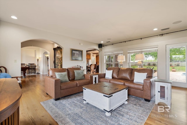 living area with recessed lighting, arched walkways, visible vents, and light wood-style floors