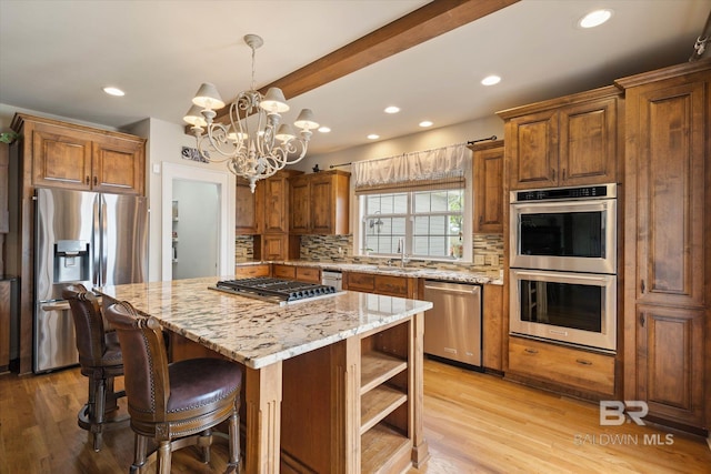kitchen with light stone countertops, decorative backsplash, stainless steel appliances, a kitchen island, and a sink