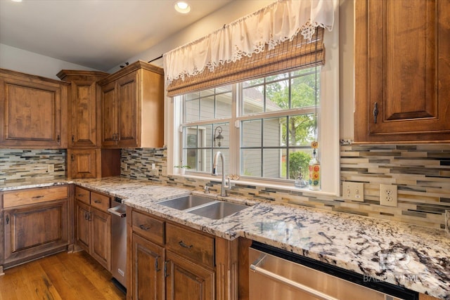 kitchen featuring tasteful backsplash, wood finished floors, stainless steel dishwasher, and a sink