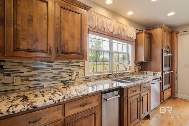 kitchen with a sink, stainless steel appliances, light stone countertops, recessed lighting, and light wood finished floors