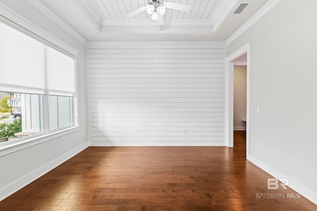 empty room featuring a tray ceiling, dark hardwood / wood-style floors, and crown molding