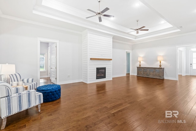 living room with crown molding, a fireplace, a raised ceiling, dark hardwood / wood-style flooring, and ceiling fan