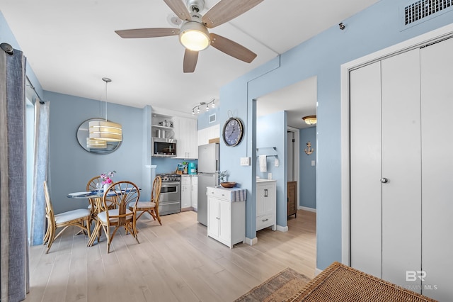 kitchen featuring appliances with stainless steel finishes, white cabinets, pendant lighting, light hardwood / wood-style floors, and ceiling fan