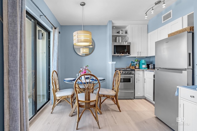 kitchen featuring decorative light fixtures, stainless steel appliances, rail lighting, white cabinets, and light hardwood / wood-style flooring