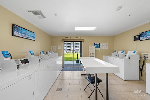 clothes washing area with washing machine and clothes dryer, ornamental molding, and light tile patterned floors