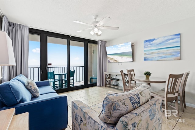 living area with ceiling fan, a wall of windows, a textured ceiling, and tile patterned floors