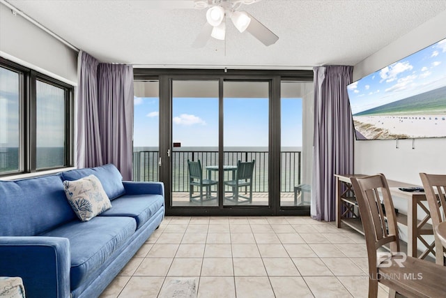 living room featuring a textured ceiling, ceiling fan, expansive windows, and light tile patterned flooring