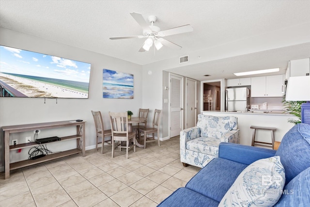 living room with a textured ceiling, light tile patterned flooring, visible vents, baseboards, and a ceiling fan