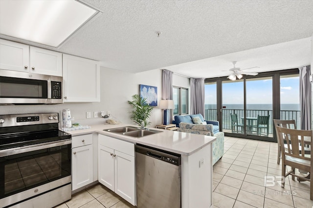 kitchen with stainless steel appliances, a peninsula, a sink, white cabinetry, and light countertops