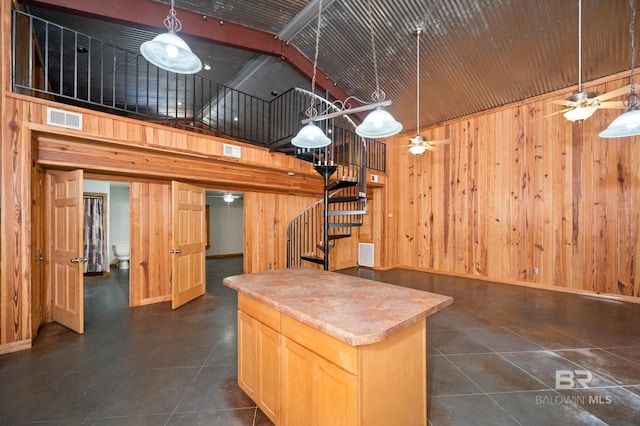 kitchen featuring ceiling fan, light brown cabinetry, a high ceiling, and wood walls