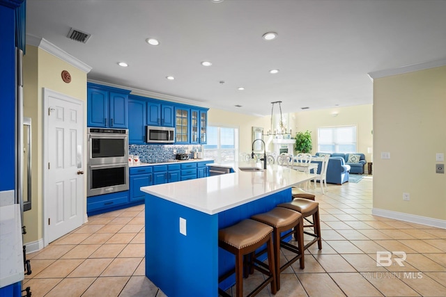 kitchen with light countertops, appliances with stainless steel finishes, blue cabinetry, an island with sink, and glass insert cabinets