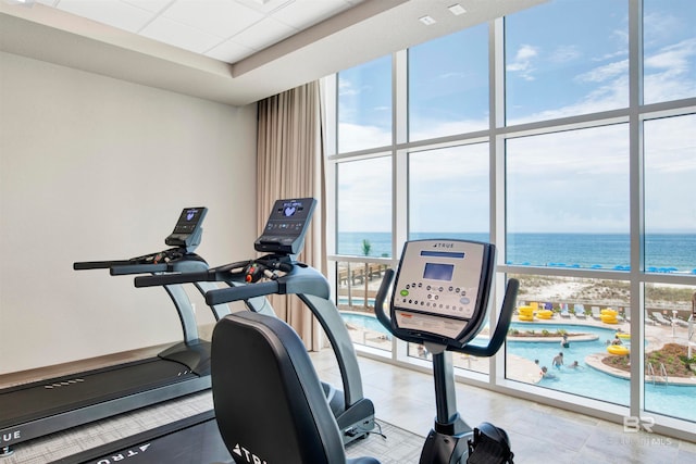 gym featuring a wall of windows, a water view, and a view of the beach