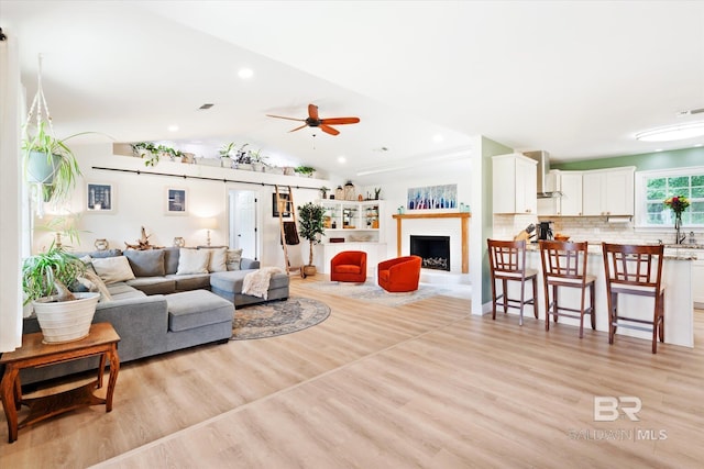 living room featuring a ceiling fan, lofted ceiling, a fireplace, and light wood finished floors