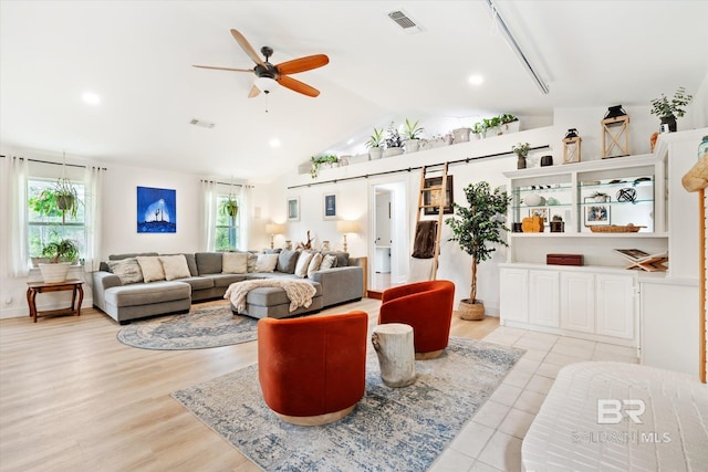 living area featuring visible vents, light wood-type flooring, a barn door, vaulted ceiling, and a ceiling fan