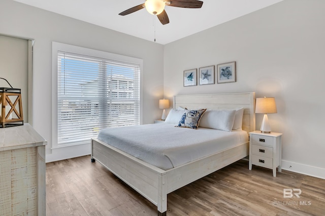 bedroom featuring ceiling fan, baseboards, multiple windows, and wood finished floors