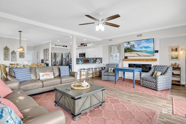 living area with a ceiling fan, crown molding, wood finished floors, and visible vents