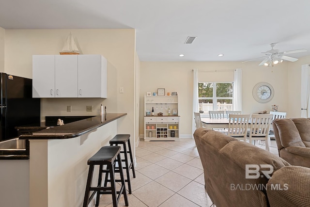 4615 Nancy Ln Unit 8, Orange Beach, AL 36561 - kitchen with light tile patterned flooring, a kitchen bar, black fridge, kitchen peninsula, and white cabinets