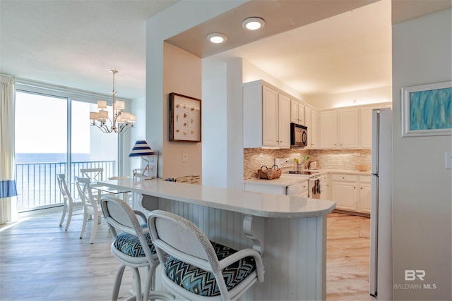 kitchen featuring white cabinets, light hardwood / wood-style flooring, tasteful backsplash, a notable chandelier, and stainless steel appliances