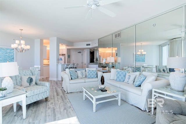 living room with ceiling fan with notable chandelier and light hardwood / wood-style flooring