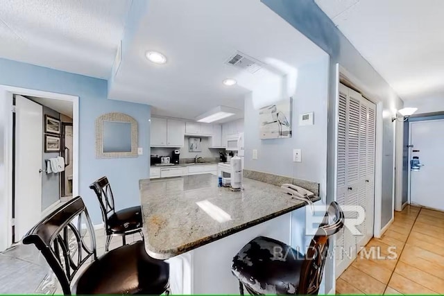 kitchen featuring white cabinetry, dark stone counters, a kitchen breakfast bar, and kitchen peninsula