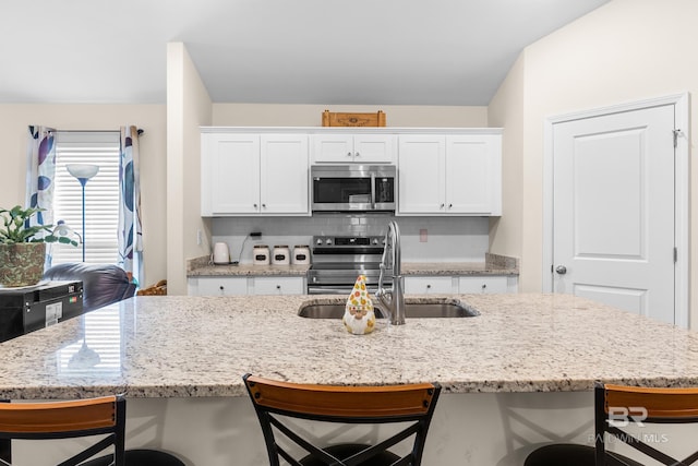 kitchen featuring stainless steel appliances, white cabinetry, a breakfast bar area, and sink