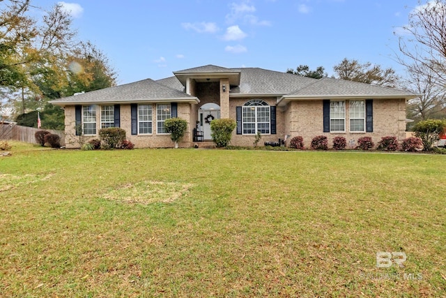 view of front of house featuring brick siding, roof with shingles, a front yard, and fence