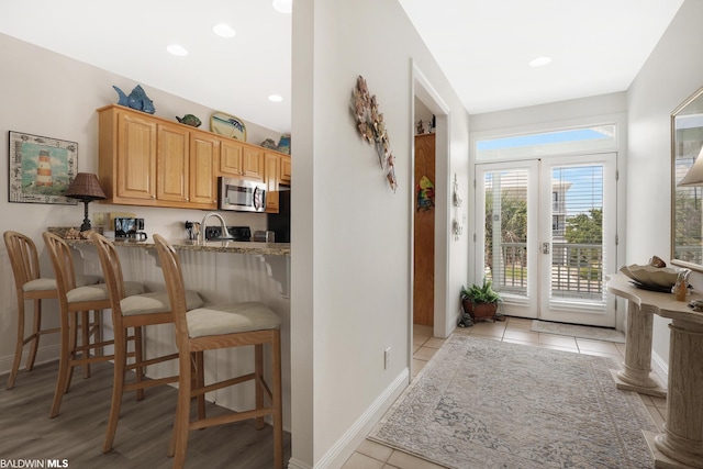 kitchen with a kitchen bar, sink, light tile floors, and light stone counters