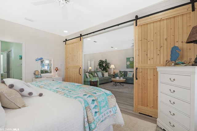 bedroom with a barn door, ceiling fan, and light hardwood / wood-style flooring