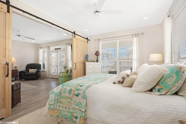 bedroom with a barn door, multiple windows, ceiling fan, and wood-type flooring